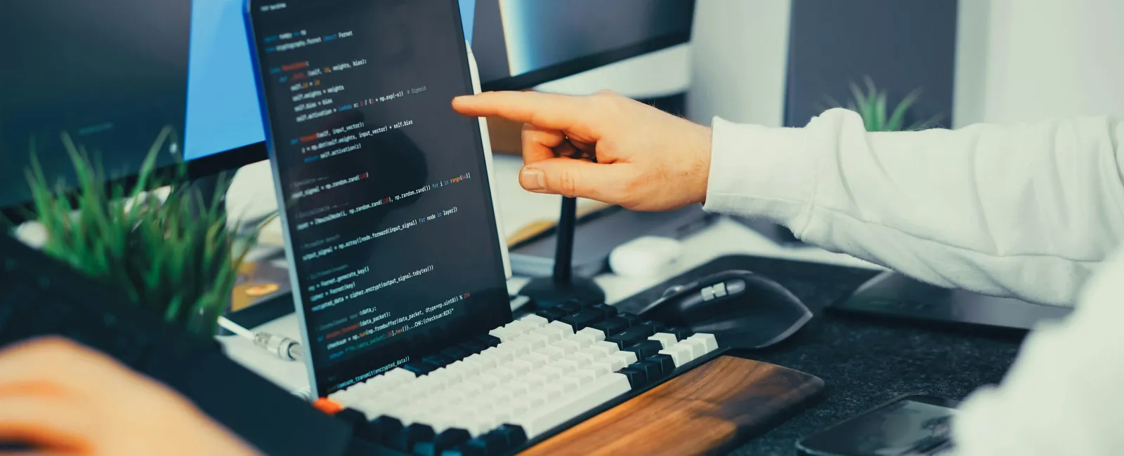 Developer pointing at code on a tablet screen at a modern workspace with keyboard and monitors.
