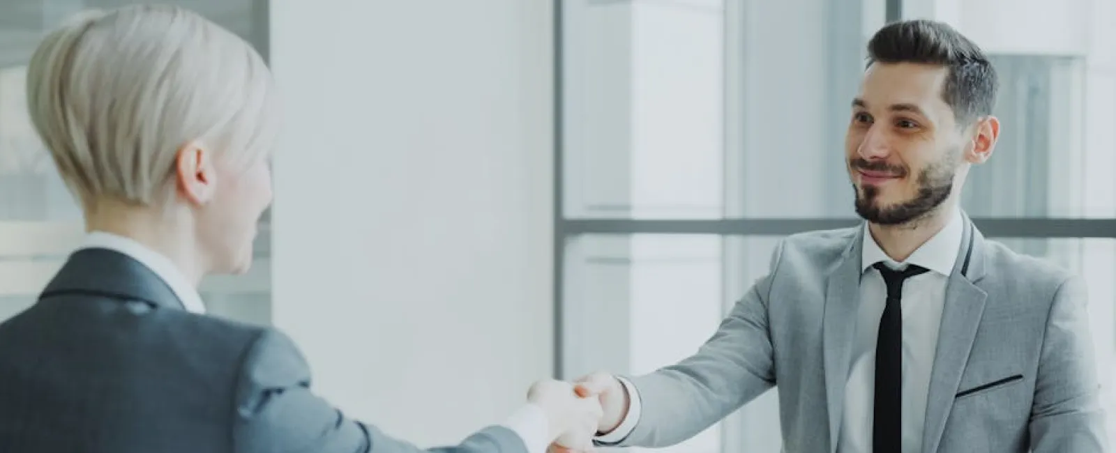 Two business professionals shaking hands during a meeting in a modern office setting.