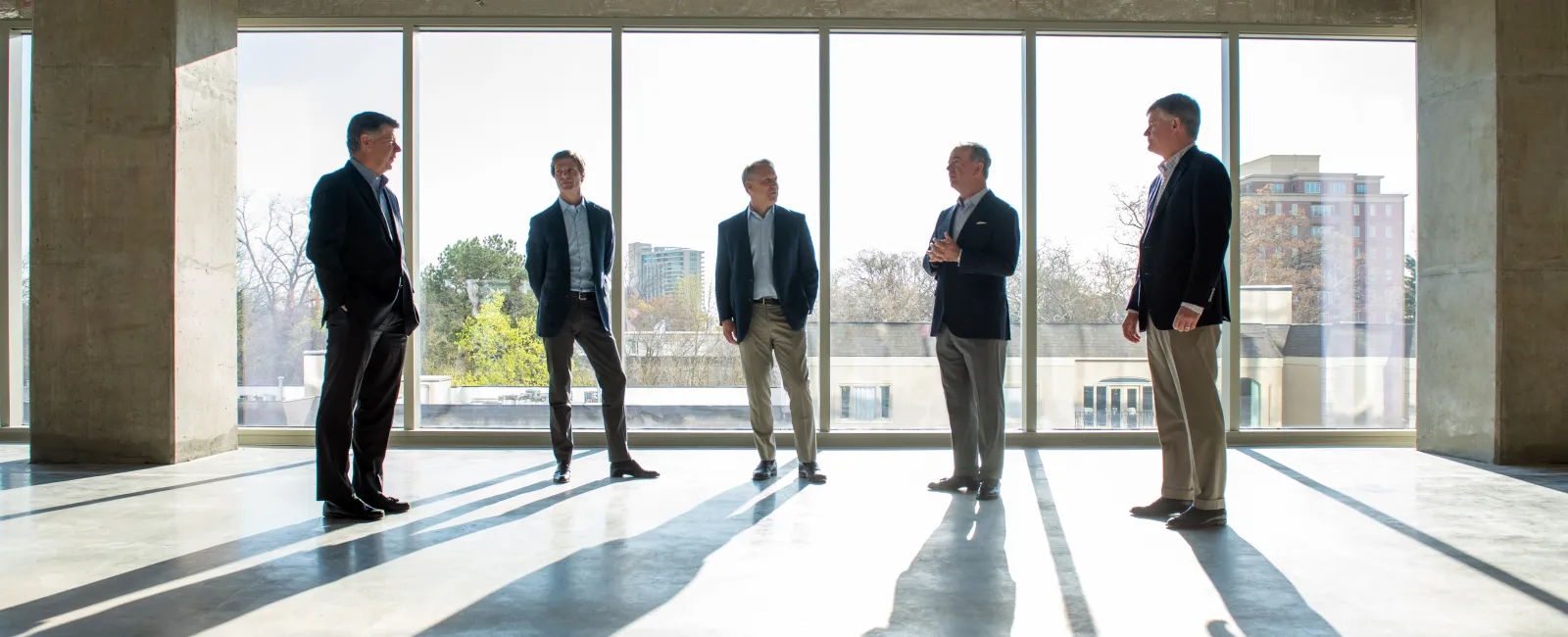 a group of men standing in a room with large windows