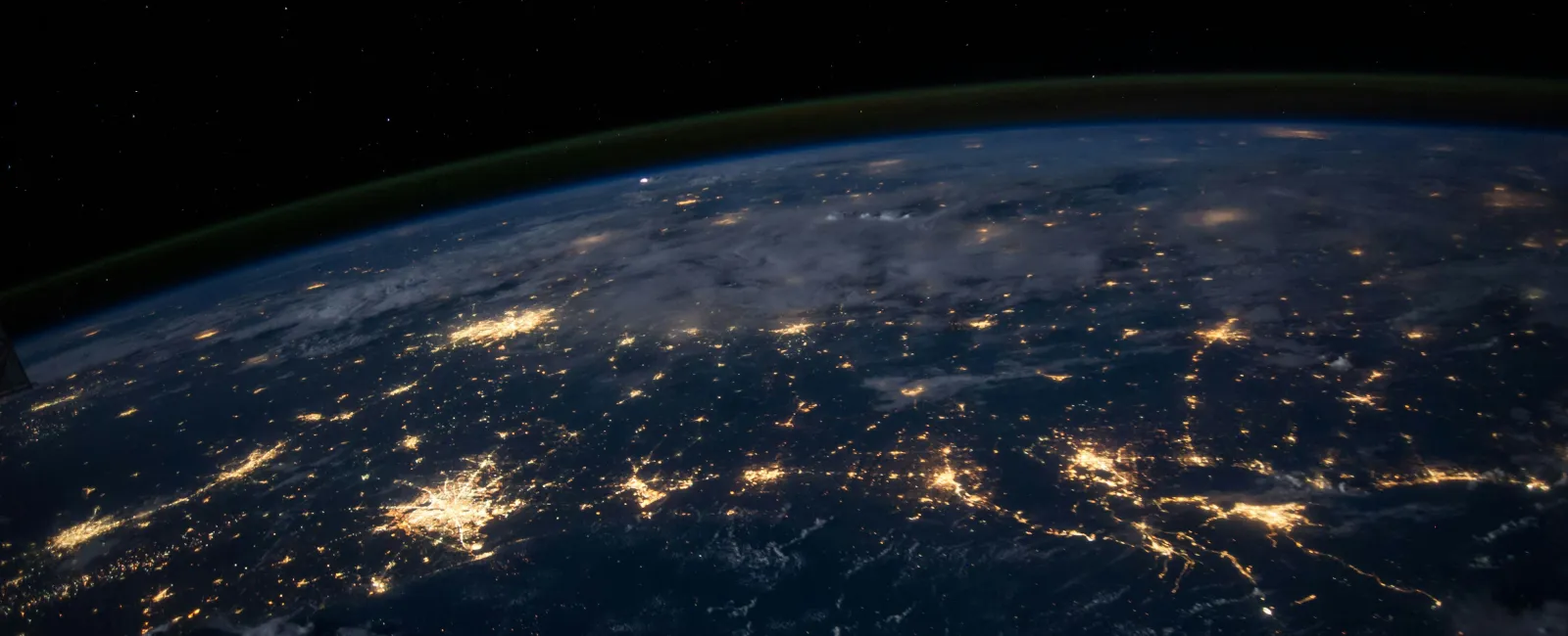 Bright city lights glow across Earth's surface at night, visible from space against the dark cosmos.