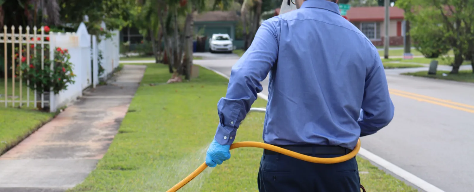 Pest control technician in blue uniform spraying outside a house lawn with safety gloves and goggles.