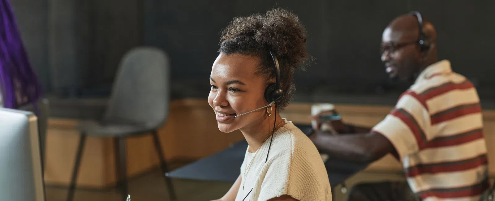 Young woman wearing headset working at a computer and taking notes in a modern office environment
