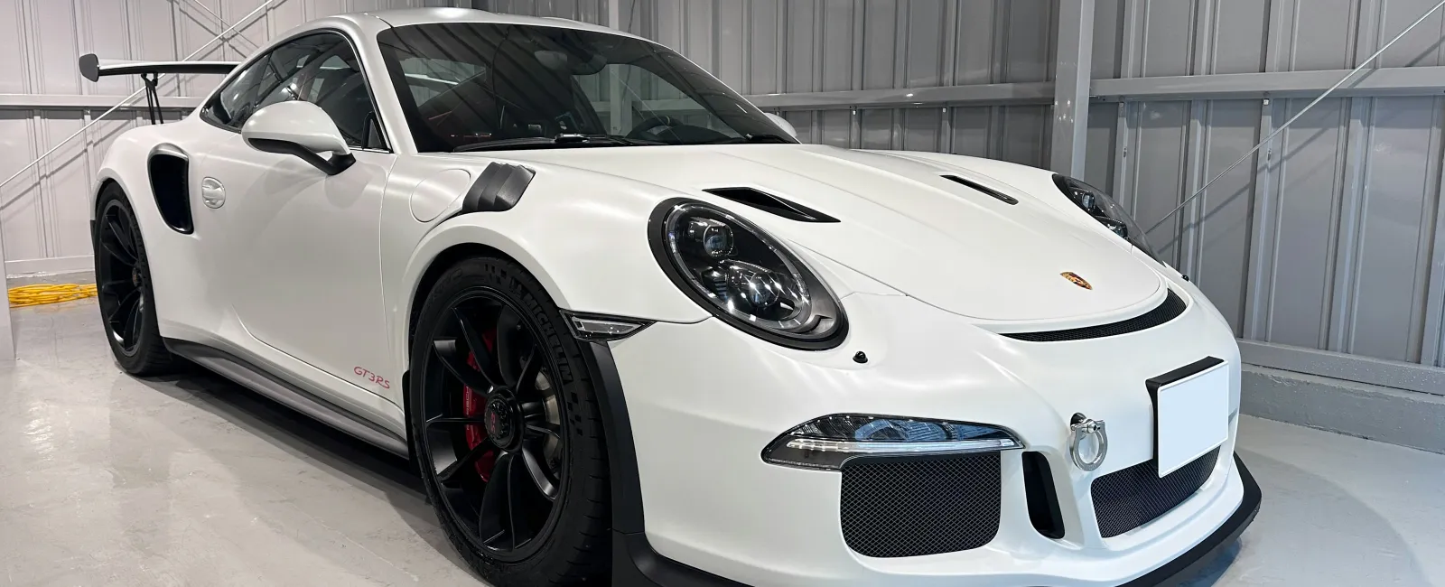 White Porsche 911 GT3 RS sports car with black rims in a bright modern garage showroom.