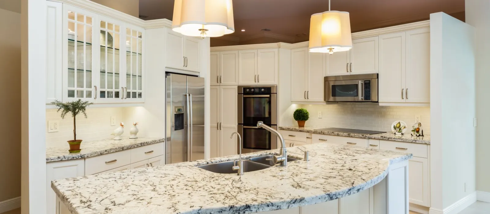 Modern kitchen with white cabinets, granite island countertop, double sink, stainless steel appliances, and pendant lights