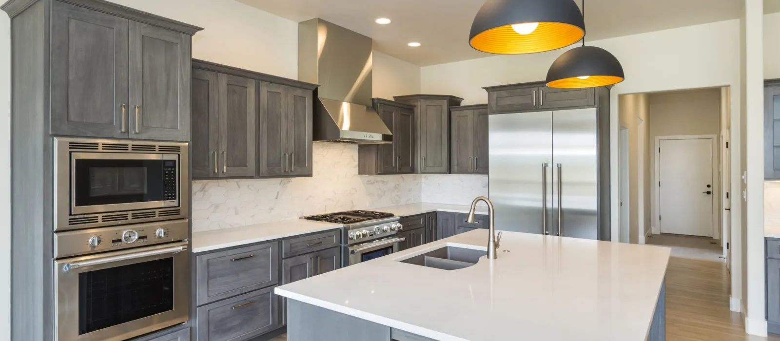 Modern kitchen with gray cabinets, white island countertop, stainless steel appliances, and pendant lighting.