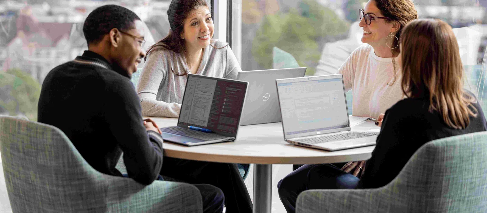 Group of professionals collaborating at a round table with laptops in a bright office space.