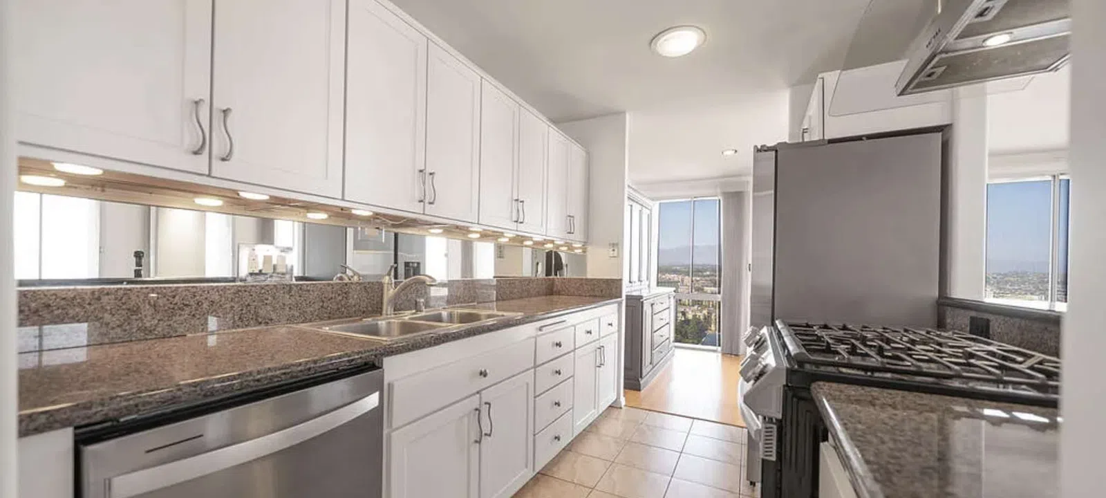 Modern kitchen with white cabinets, granite countertops, stainless steel appliances, and large windows with city views.