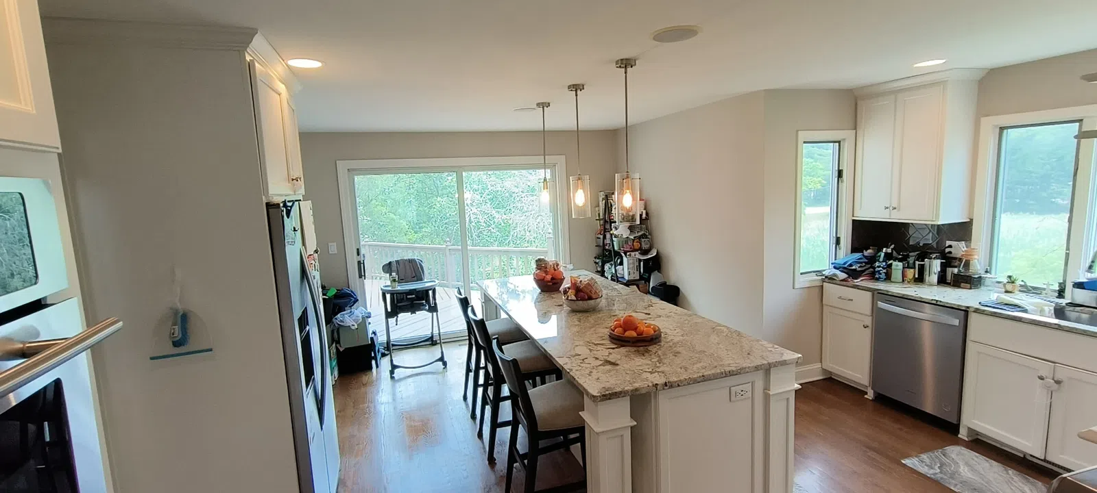 Modern kitchen with white cabinets, marble island, hardwood flooring, stainless steel appliances, and large sliding glass doors.