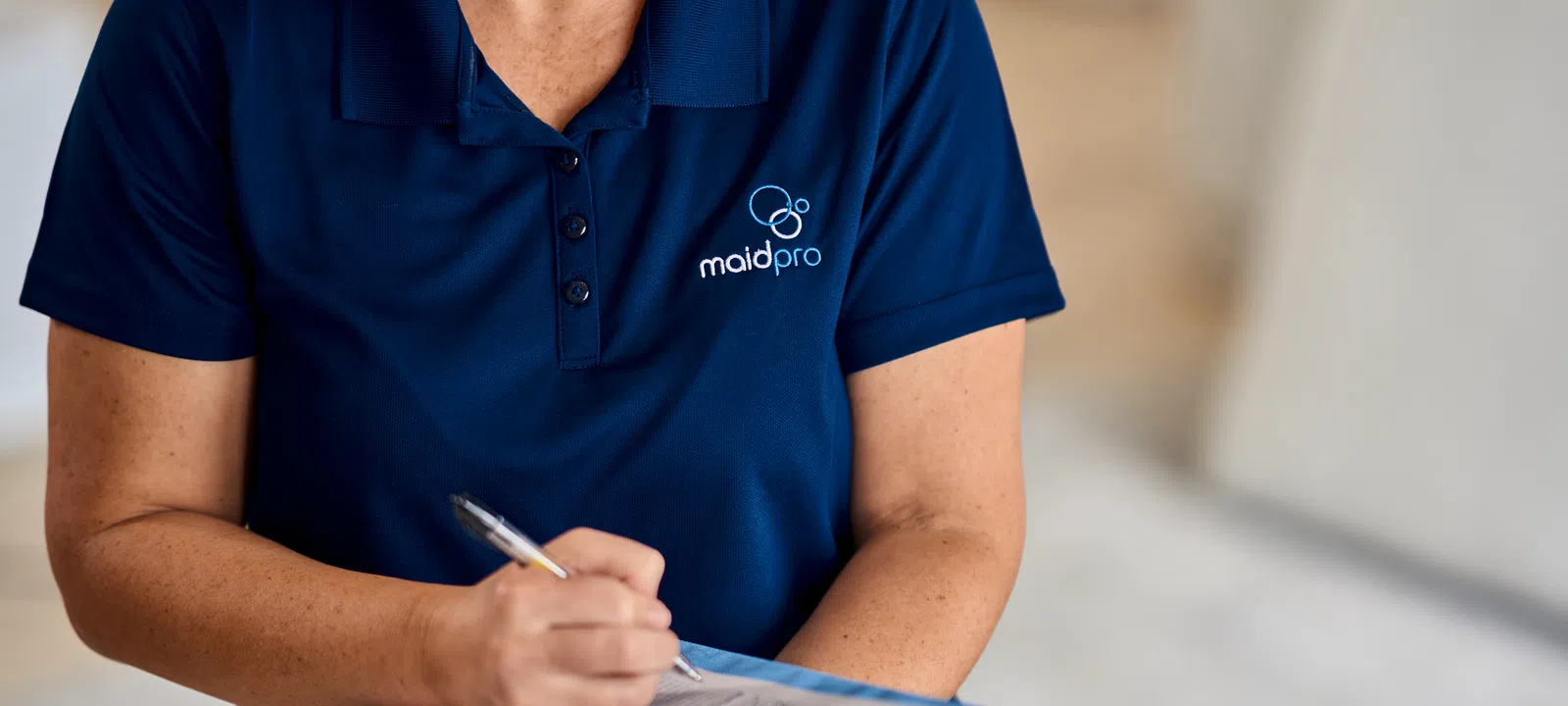 MaidPro employee in blue polo shirt writing on a clipboard during a commercial cleaning service.