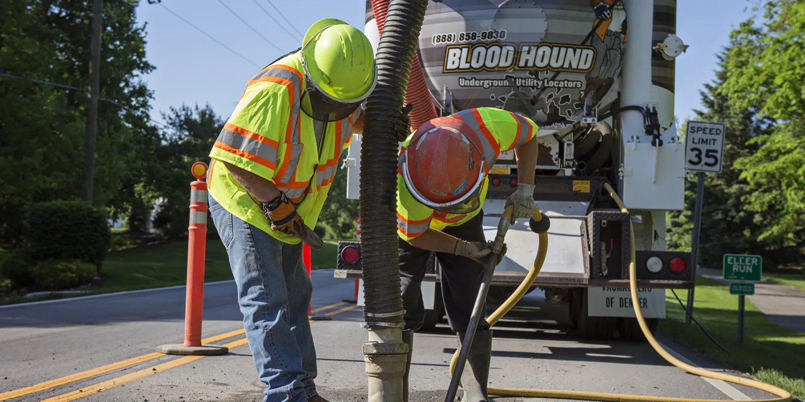 Two men from Blood Hound Underground Utility Locators working with a vacuum excavation truck