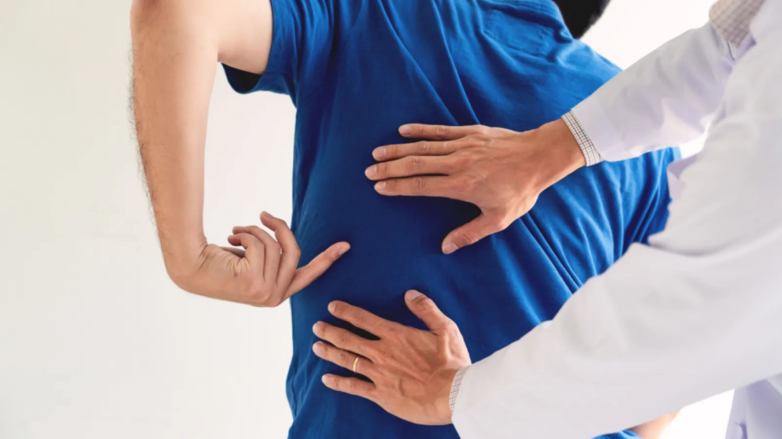 Doctor examining patient's lower back pain during a medical consultation in a clinical setting.