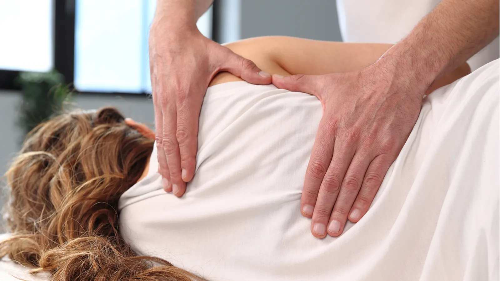Therapist performing leg and back massage on client lying face down on a massage table.