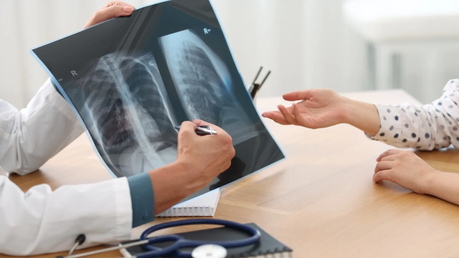 Doctor reviewing lung X-ray images with patient during medical consultation in bright office setting.