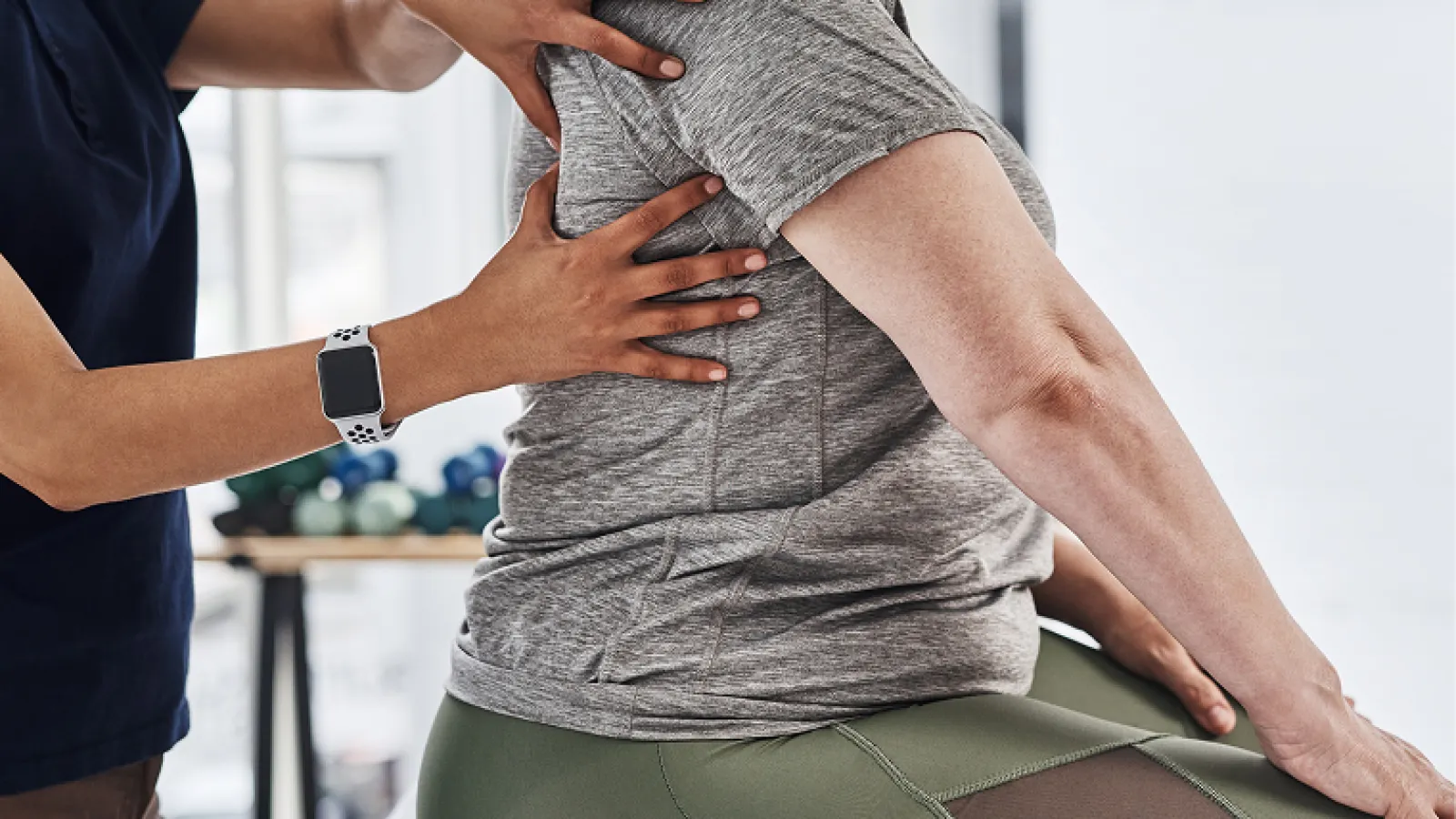Physical therapist adjusting patient's back during rehabilitation session in a bright therapy room.