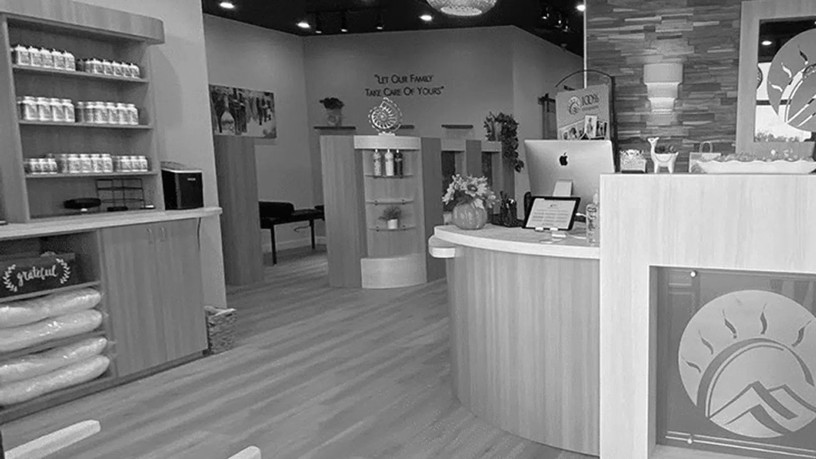 Modern wellness clinic reception area with wood finishes, computers, products, and a staff member at the desk.
