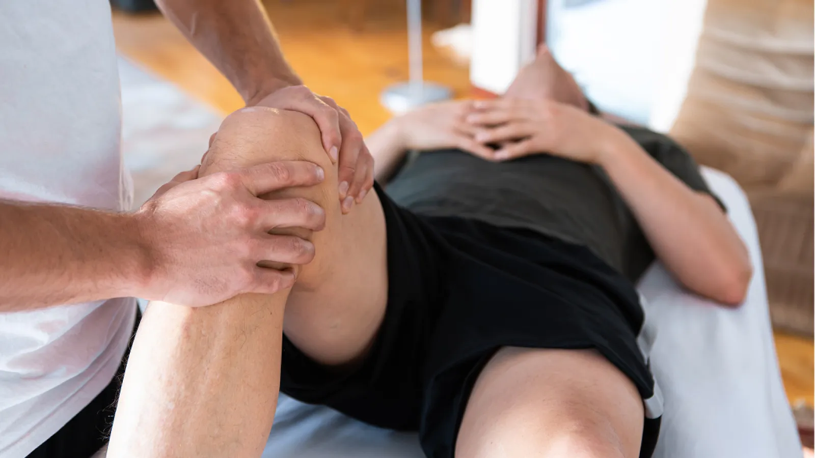 Physical therapist performing knee rehabilitation exercise on a patient lying on a treatment table.