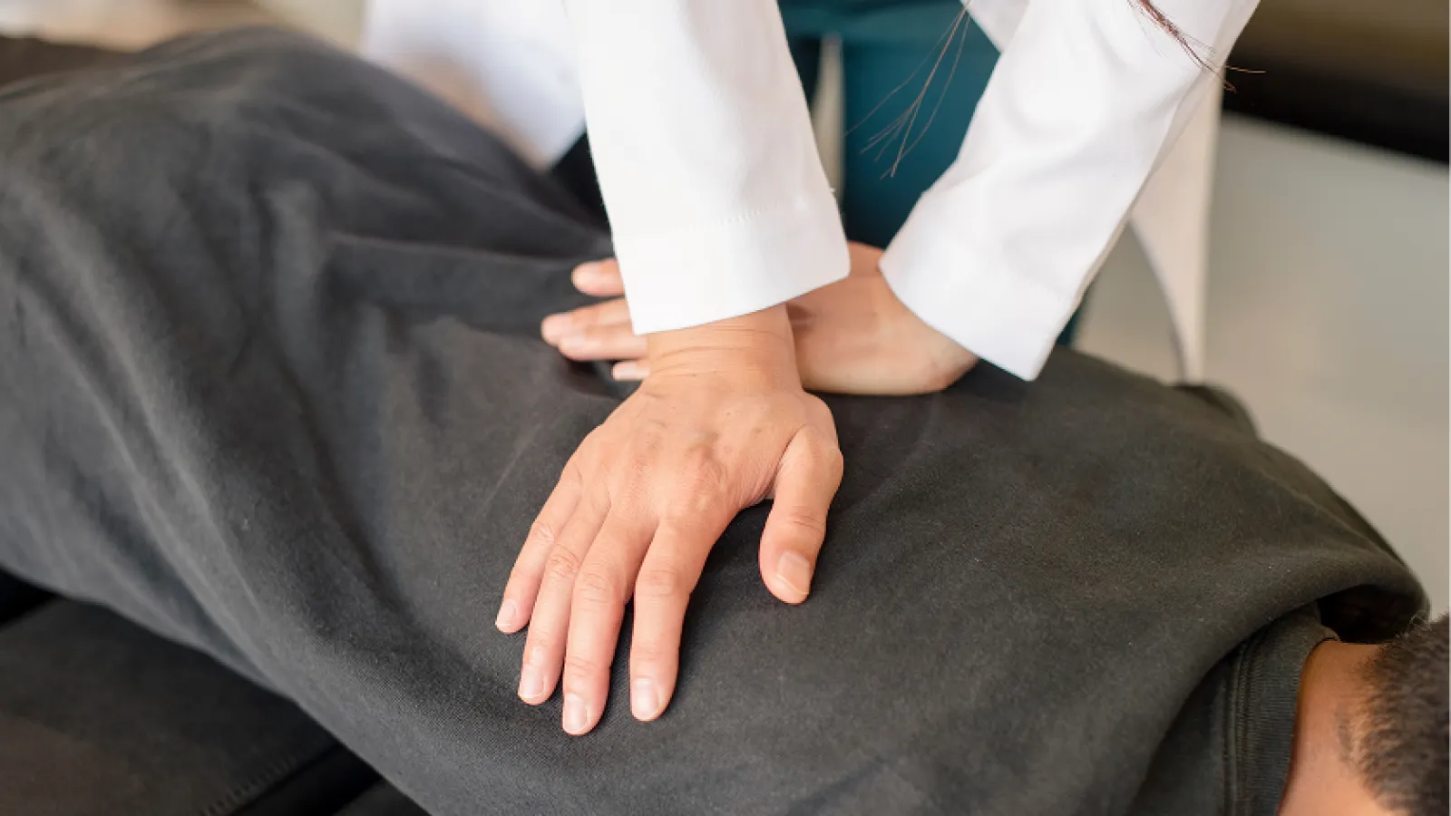 Hands performing chiropractic adjustment on a person's back wearing a black shirt on a treatment table.