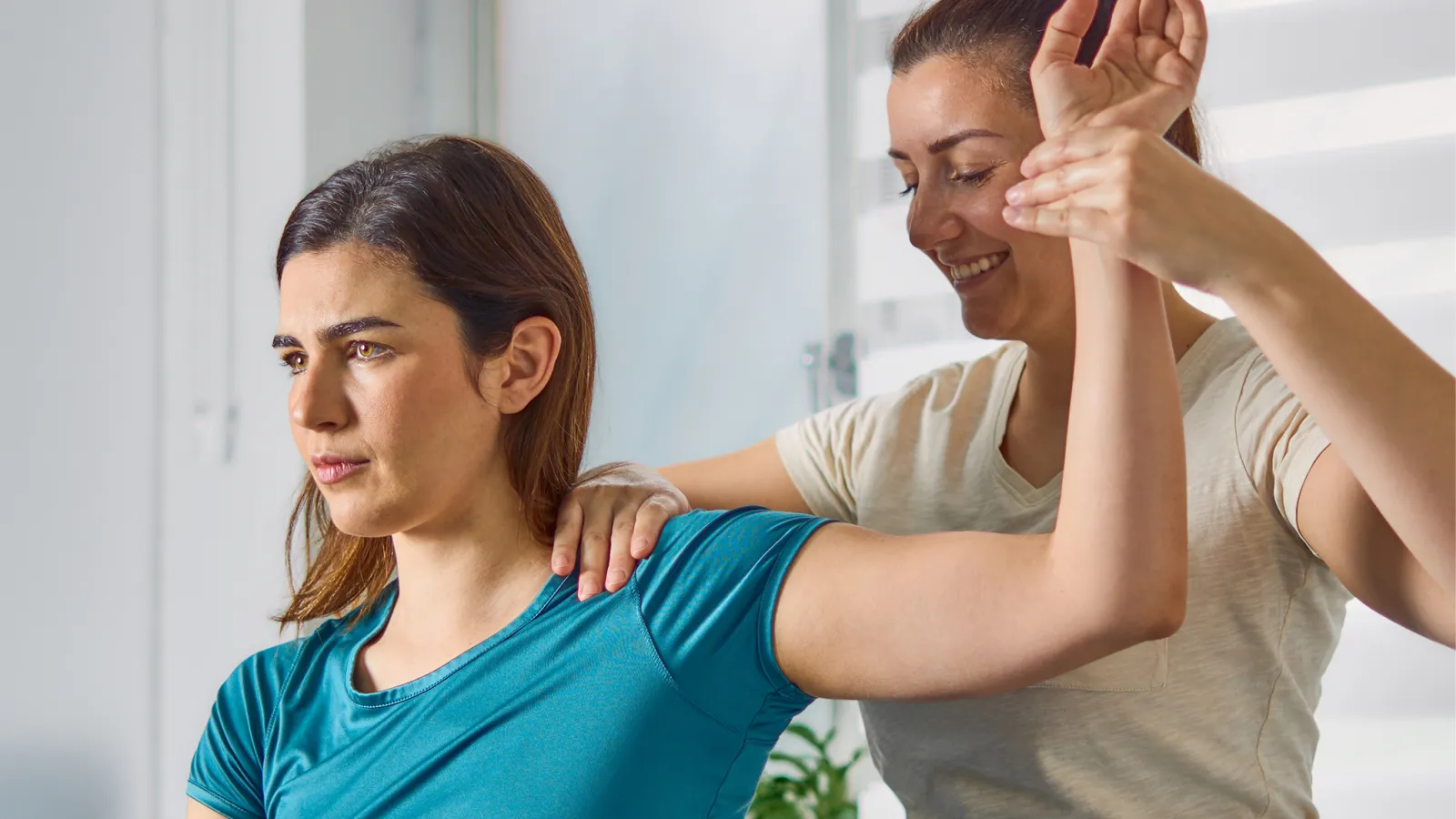 Physical therapist assisting woman with arm stretch therapy in bright room.