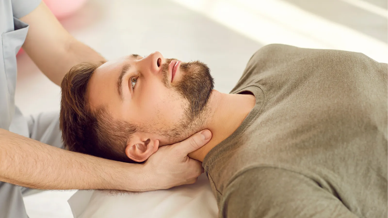 Therapist performing neck massage on a young man lying down in a calm setting.