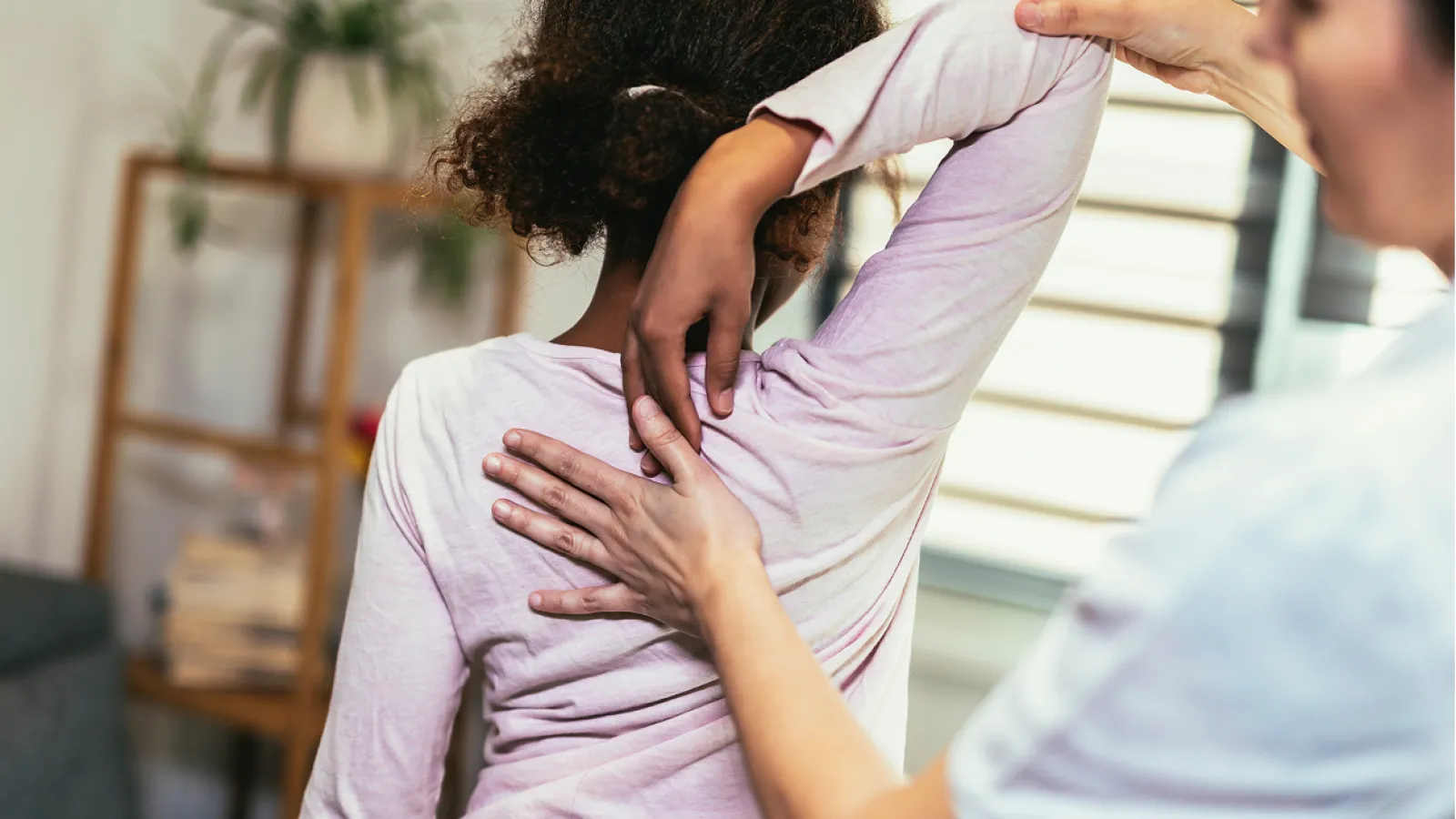 Physical therapist assisting woman with shoulder stretch in a bright room with natural light.