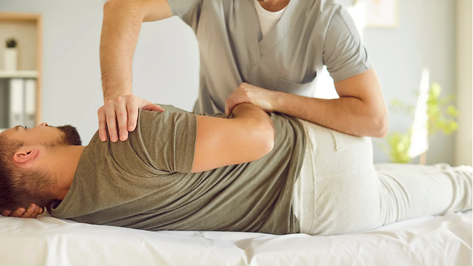 Physical therapist performing shoulder and back adjustment on a male patient lying on a treatment table.