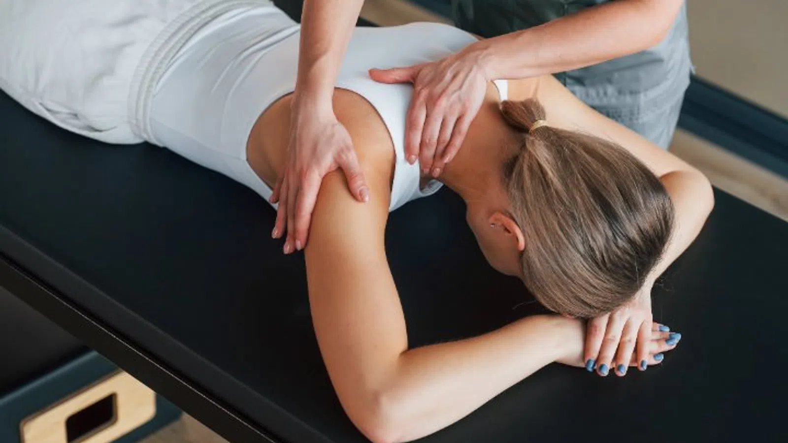 Close-up of a woman receiving a shoulder massage while lying face down on a massage table in a spa.