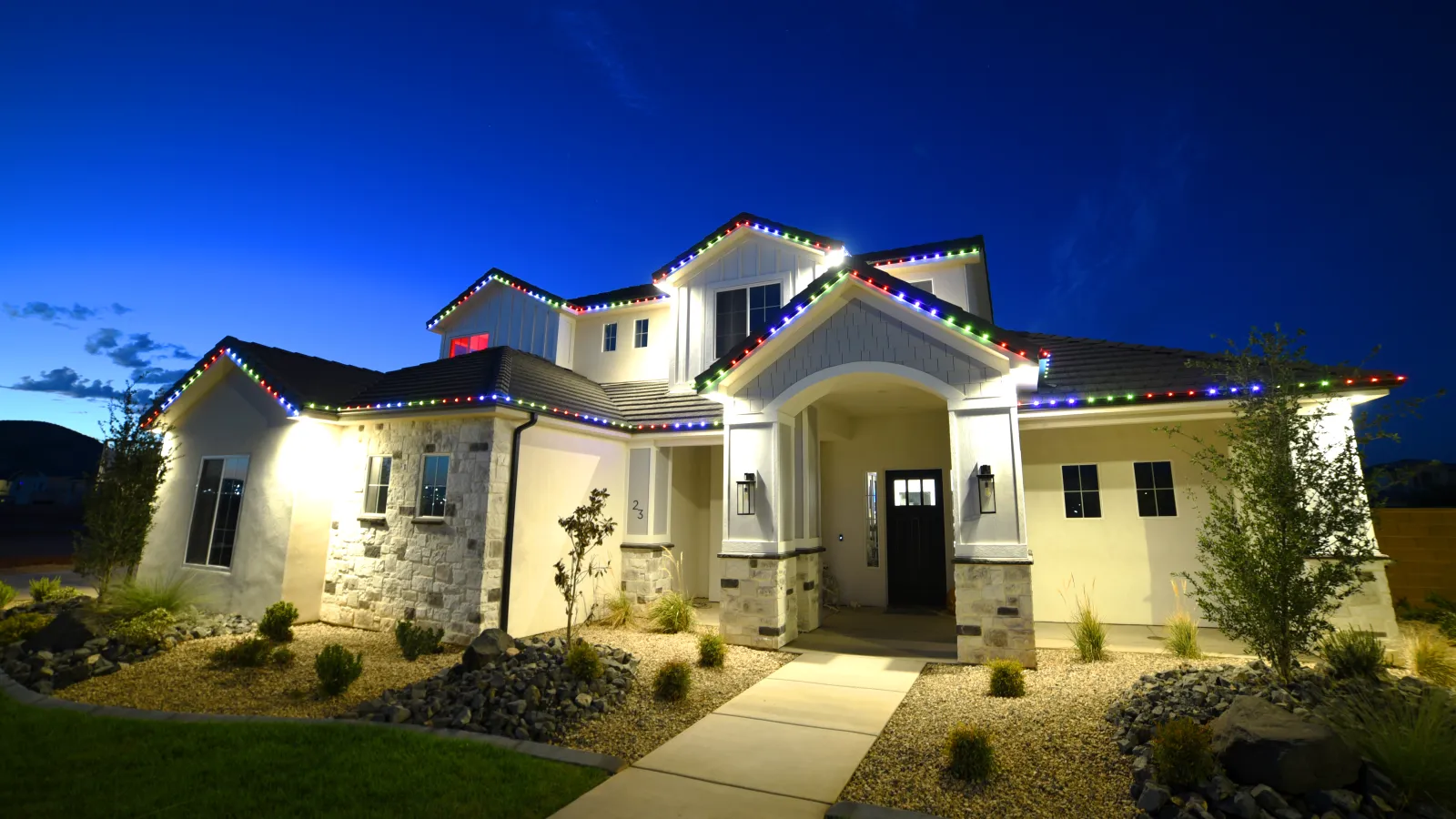 Modern house decorated with colorful Christmas lights at dusk with well-maintained front yard and pathway.