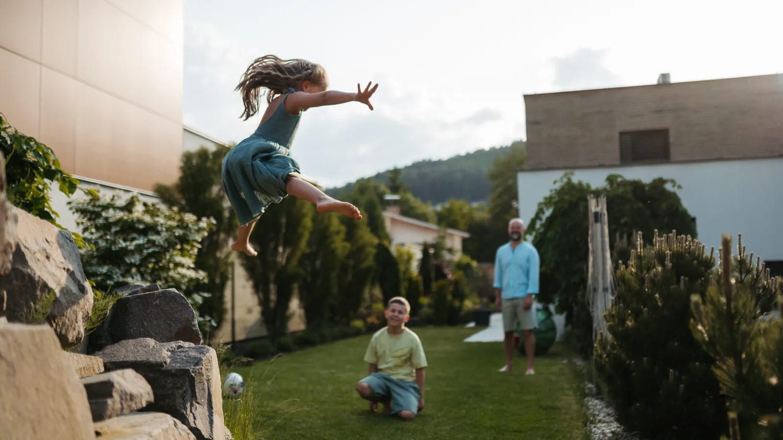 Children play in a green backyard beside a modern home on a sunny day