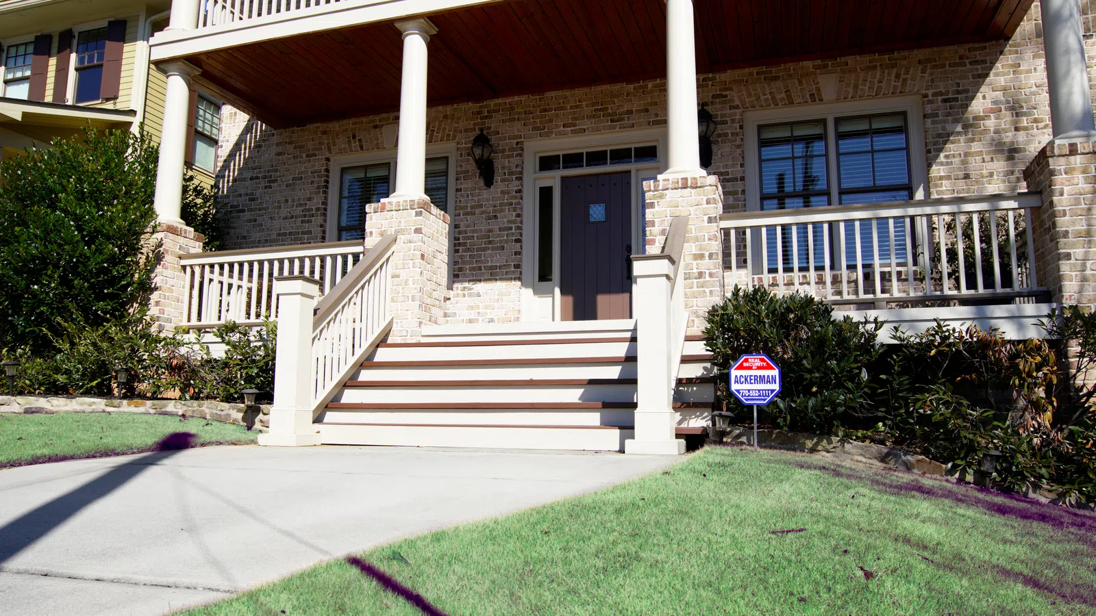 Front view of a brick house with white pillars and stairs leading to a dark wooden door.