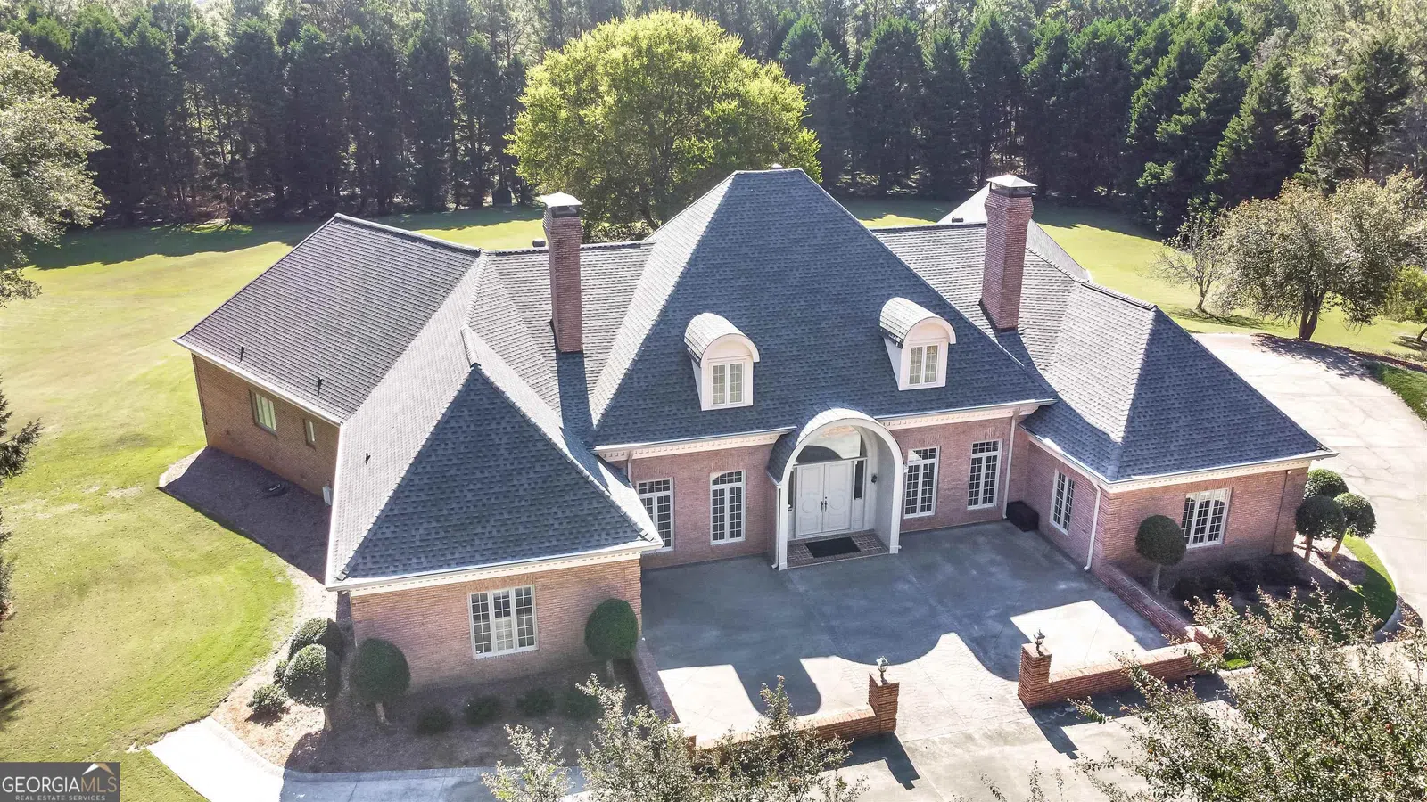 Aerial view of a spacious mansion surrounded by trees and lush landscaping.