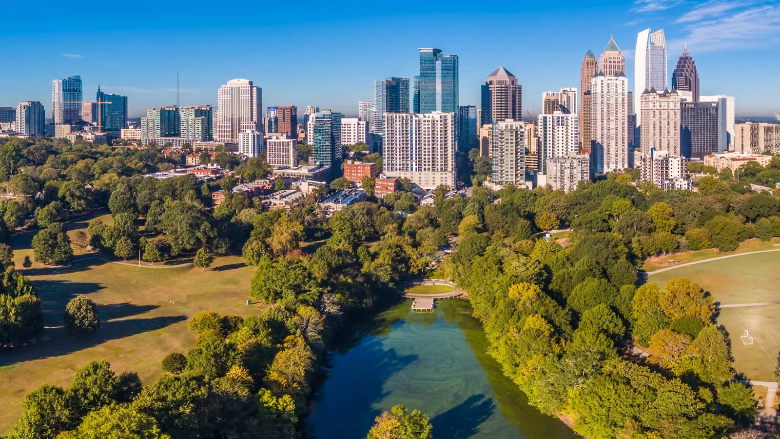 Aerial view of a city skyline with green parkland and a river running through the foreground on a clear day