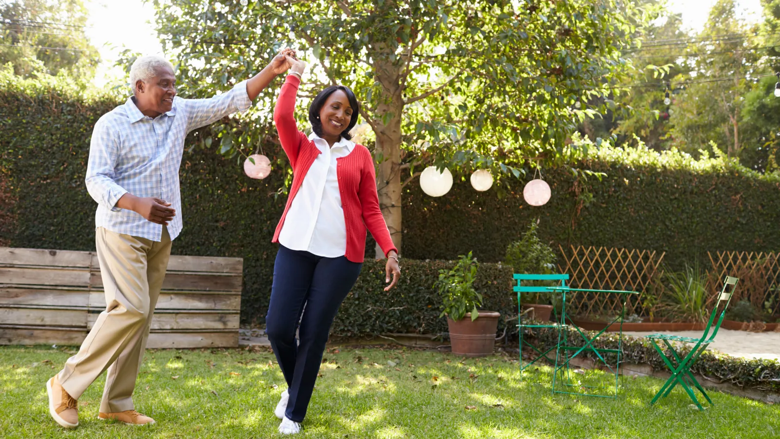 Mature couple dancing happily in sunny backyard garden with green grass and outdoor furniture
