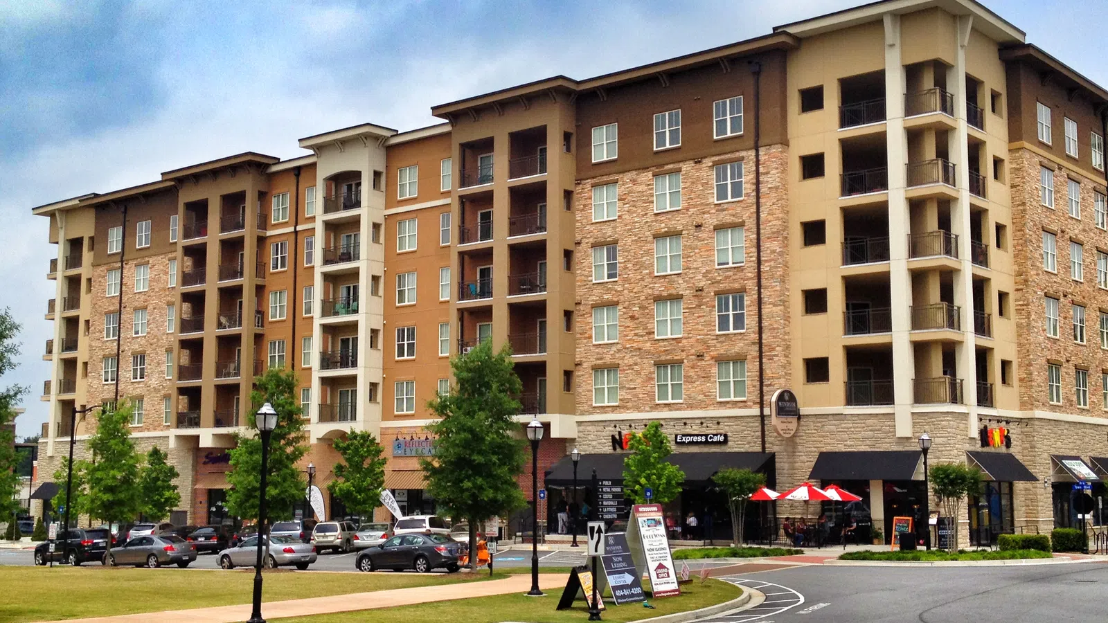 Modern apartment building with shops, green space, and cloudy sky in Brookhaven