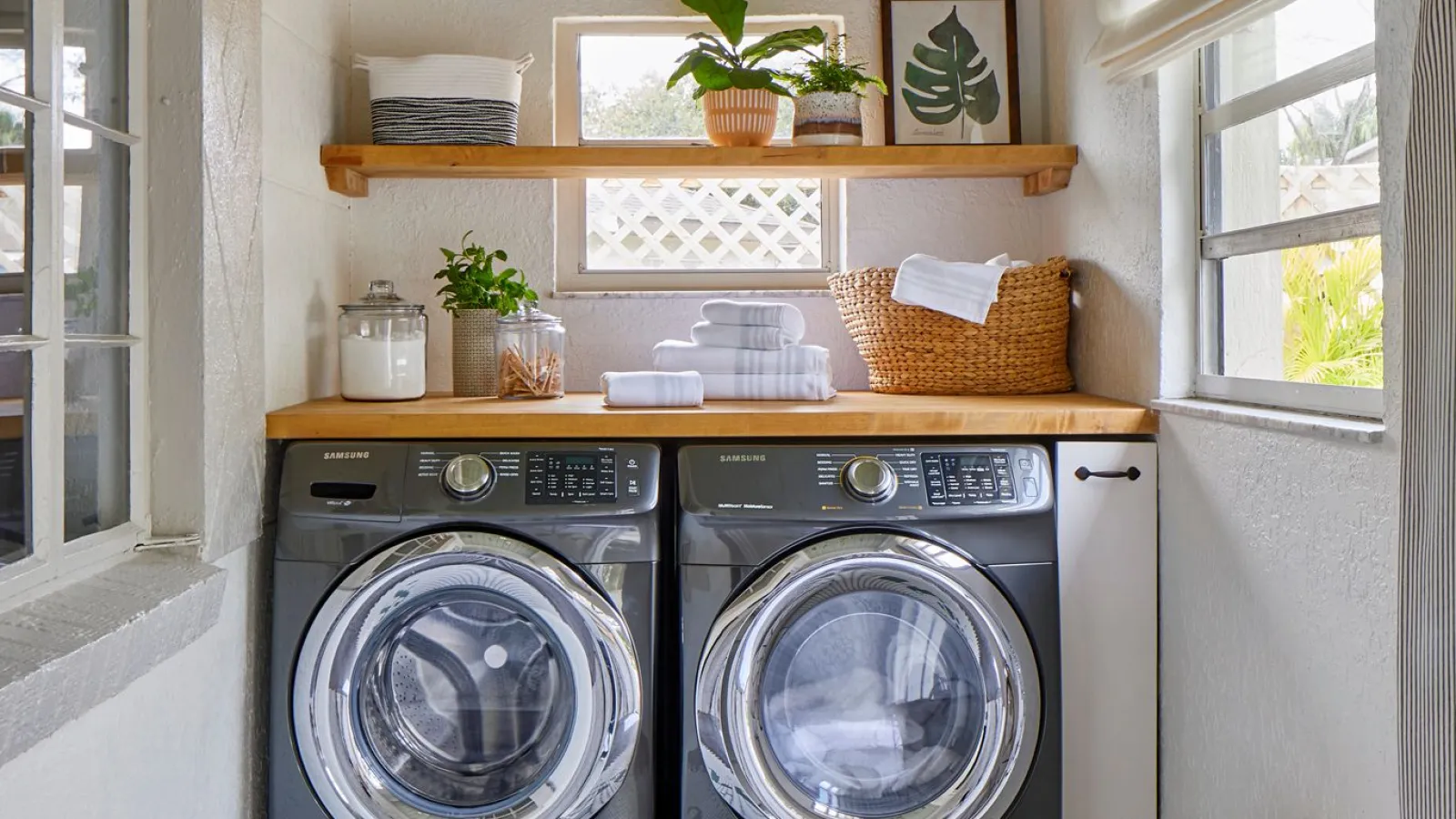 Modern laundry room with black front-loading washer and dryer, wooden shelves, plants, and tiled floor with fresh lettering.