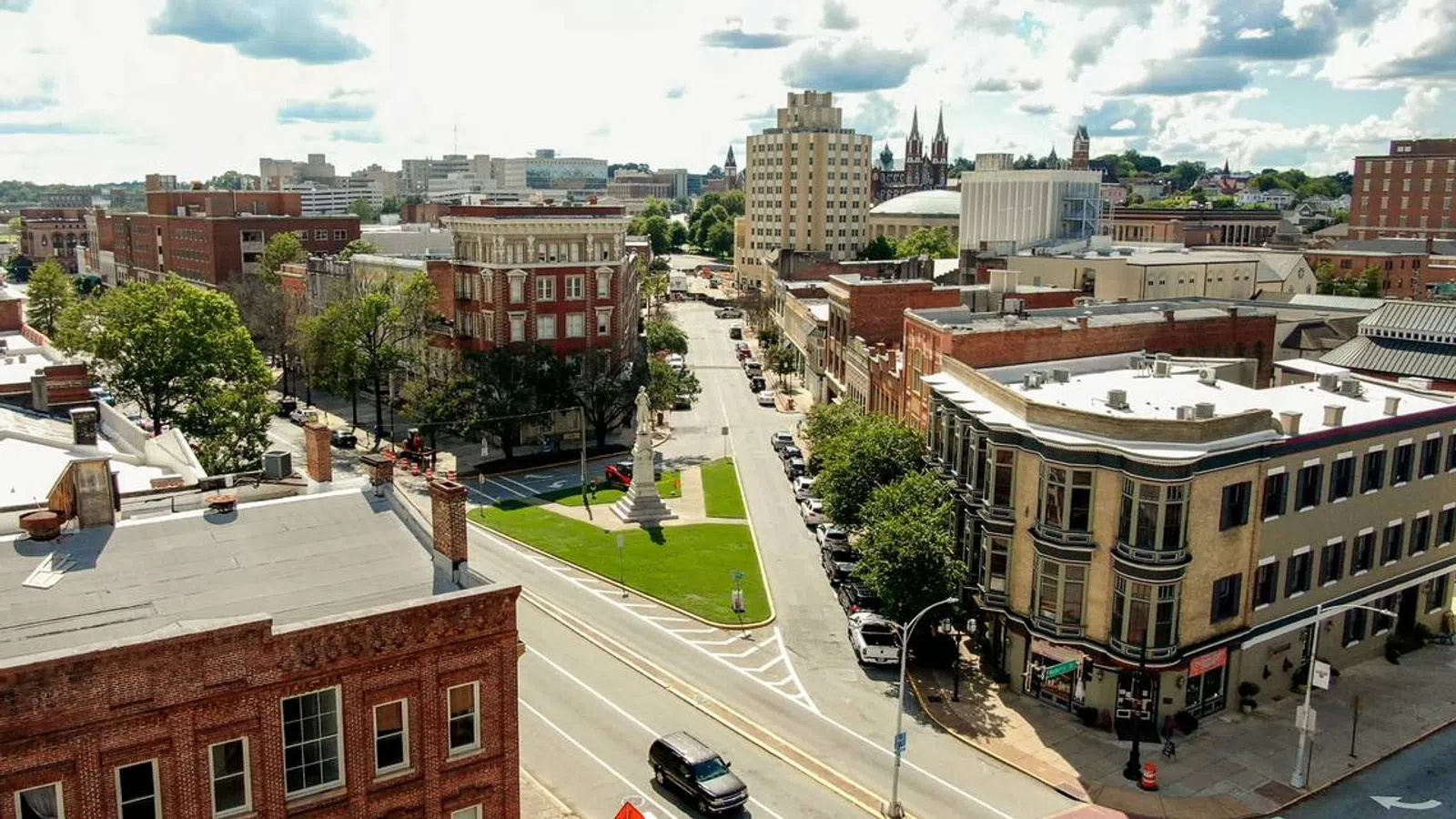 Aerial view of a downtown street with historic brick buildings, green park, and a cloudy sky.
