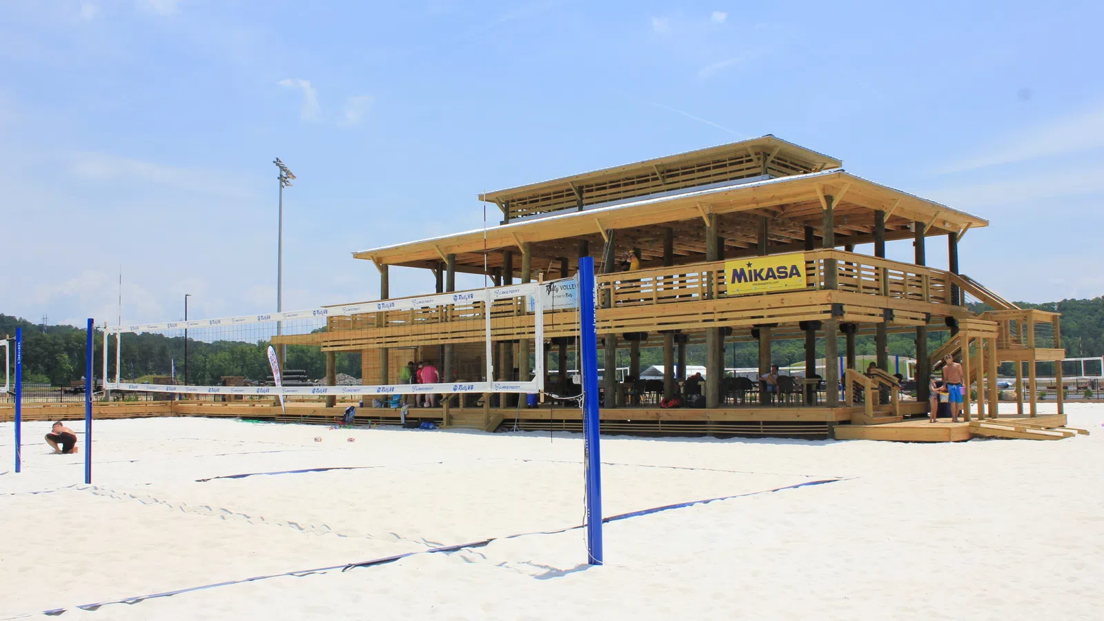 Beach volleyball courts with nets and a large wooden pavilion under a clear blue sky on sandy ground.