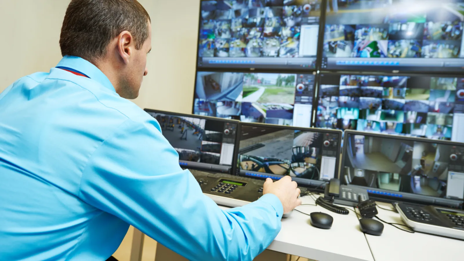 Security guard monitoring multiple surveillance camera feeds on several screens in a control room.