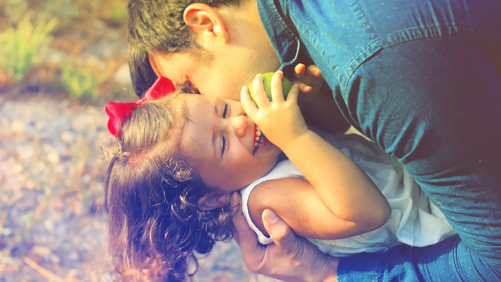 Father lovingly embraces and kisses smiling daughter outdoors