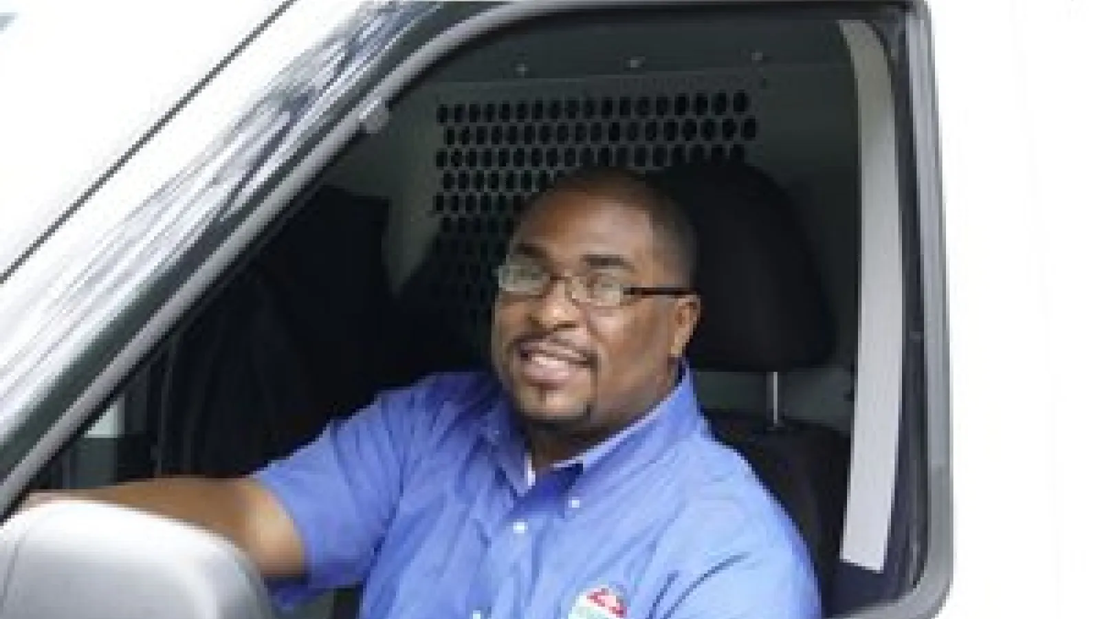 Ackerman Security man in blue uniform driving a white service van with company logo on shirt