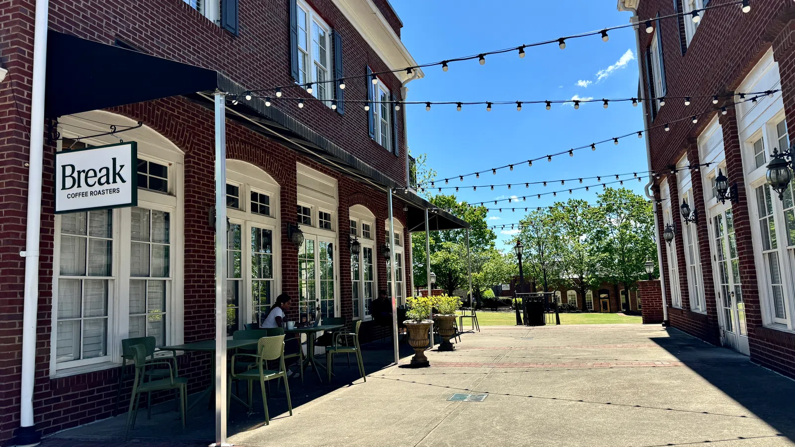 Outdoor seating area of Break Coffee Roasters with brick buildings, string lights, and clear blue sky on a sunny day.