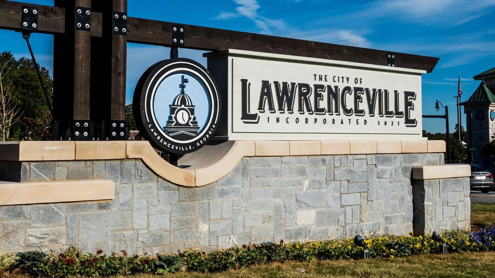 Welcome sign for the City of Lawrenceville on a stone base with clear blue sky and nearby buildings in the background
