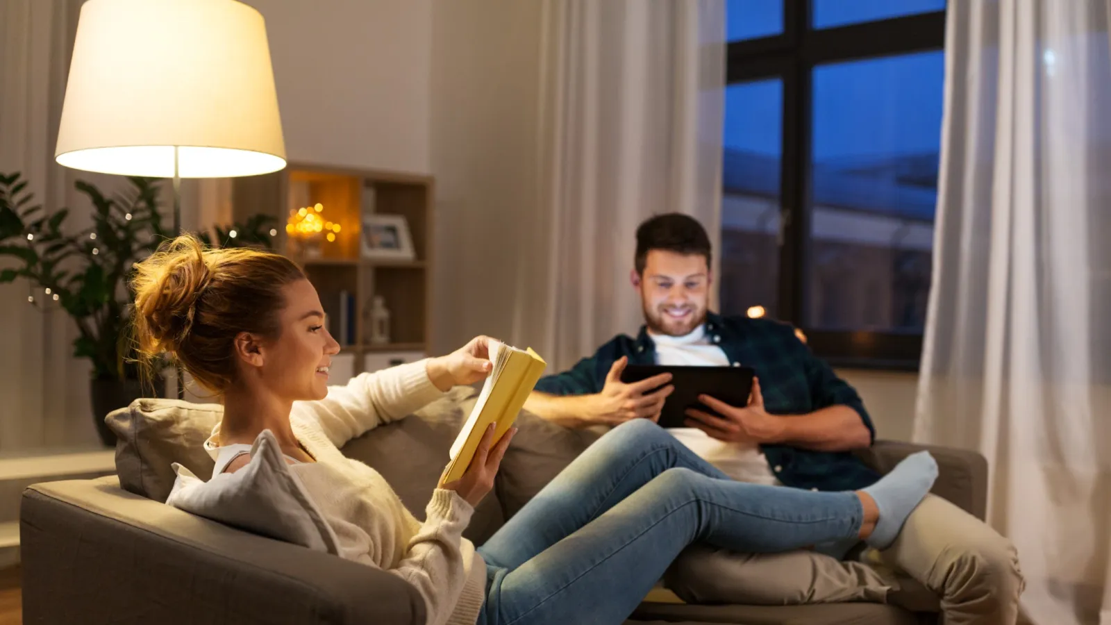 a man and a woman sitting on a couch reading a book