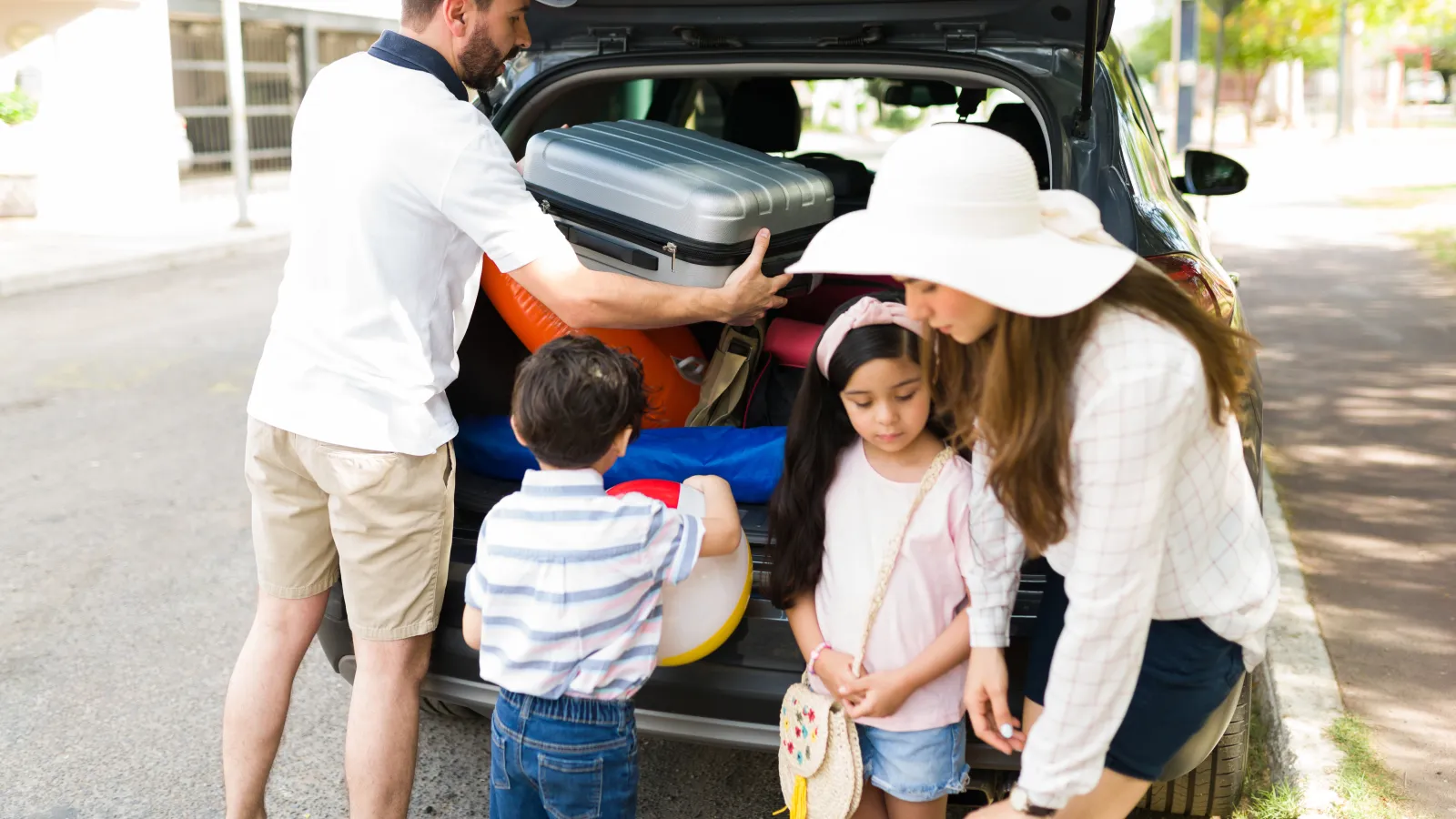 Family packing car trunk with suitcases and beach gear for vacation on a sunny day.