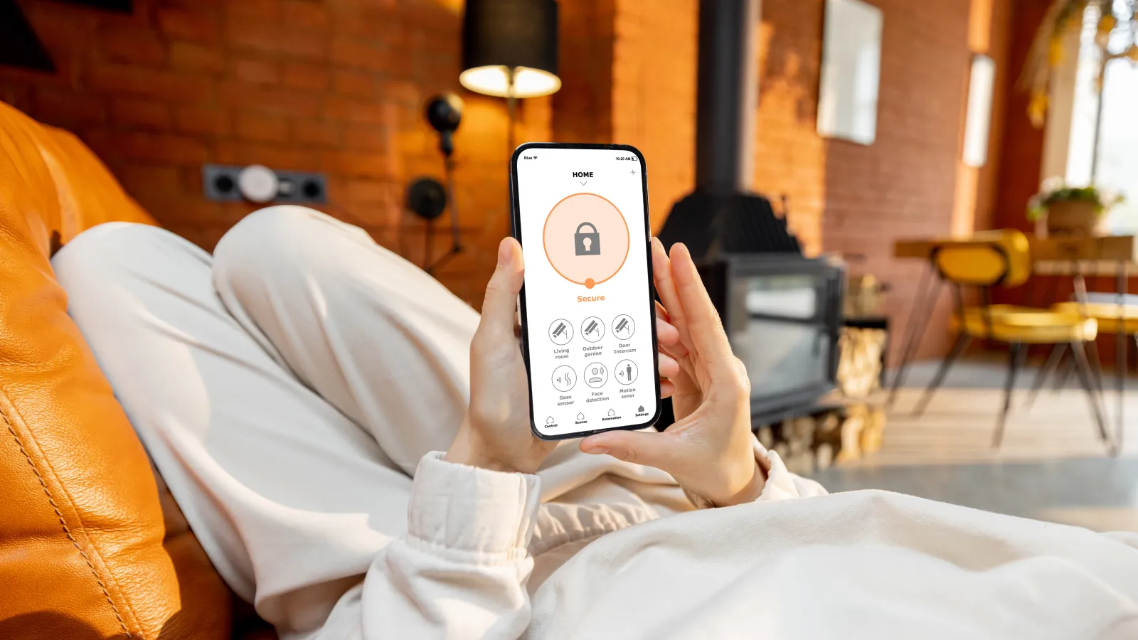 Person relaxing on couch using smartphone app to control home security system in cozy living room.