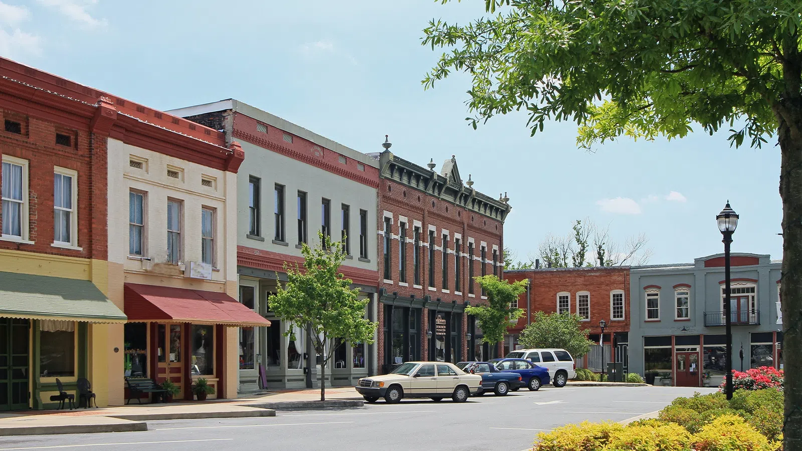 A charming small town street featuring historic buildings and green landscapes under a blue sky.