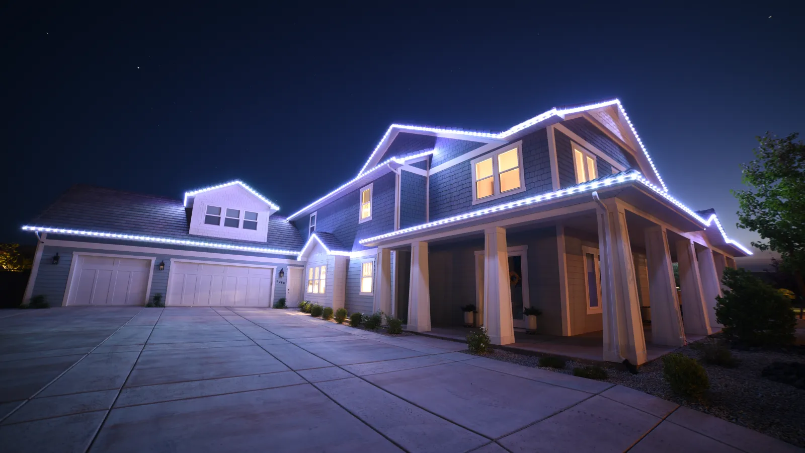 Modern two-story house at night with bright white LED lights outlining the roof and garage doors under a starry sky