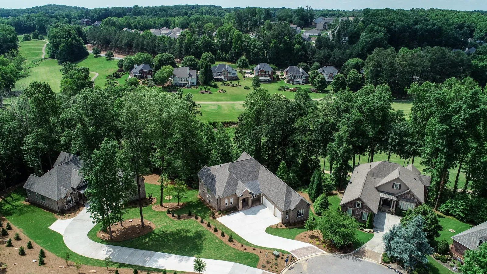 Aerial view of suburban houses surrounded by trees with a golf course and more homes in the background