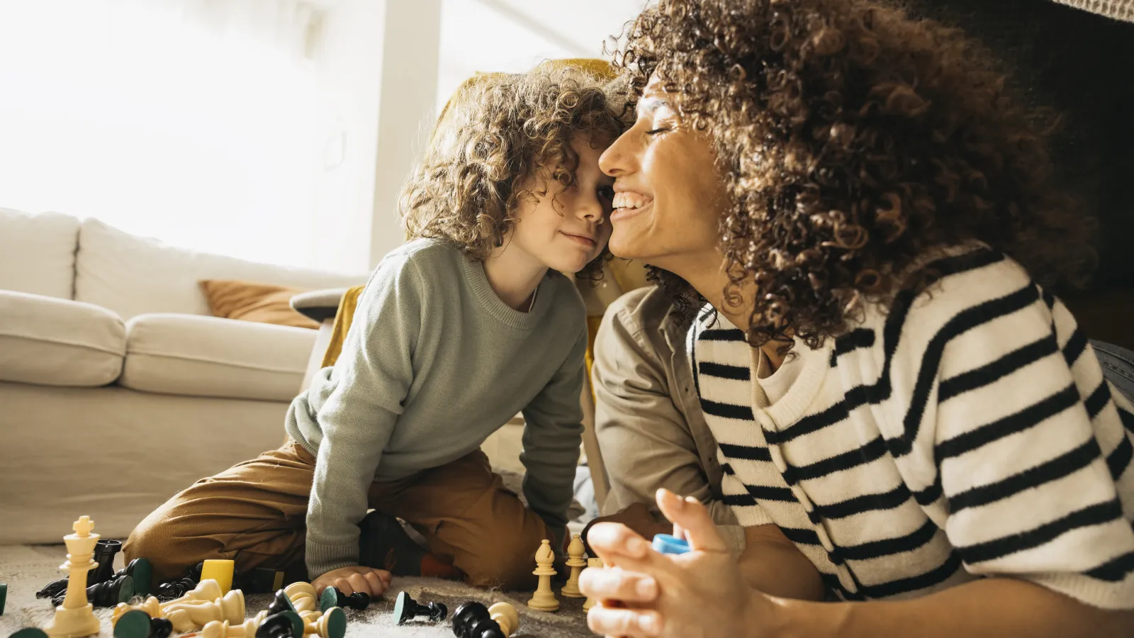 Mother and son sharing a joyful moment while playing chess on the floor in a bright living room