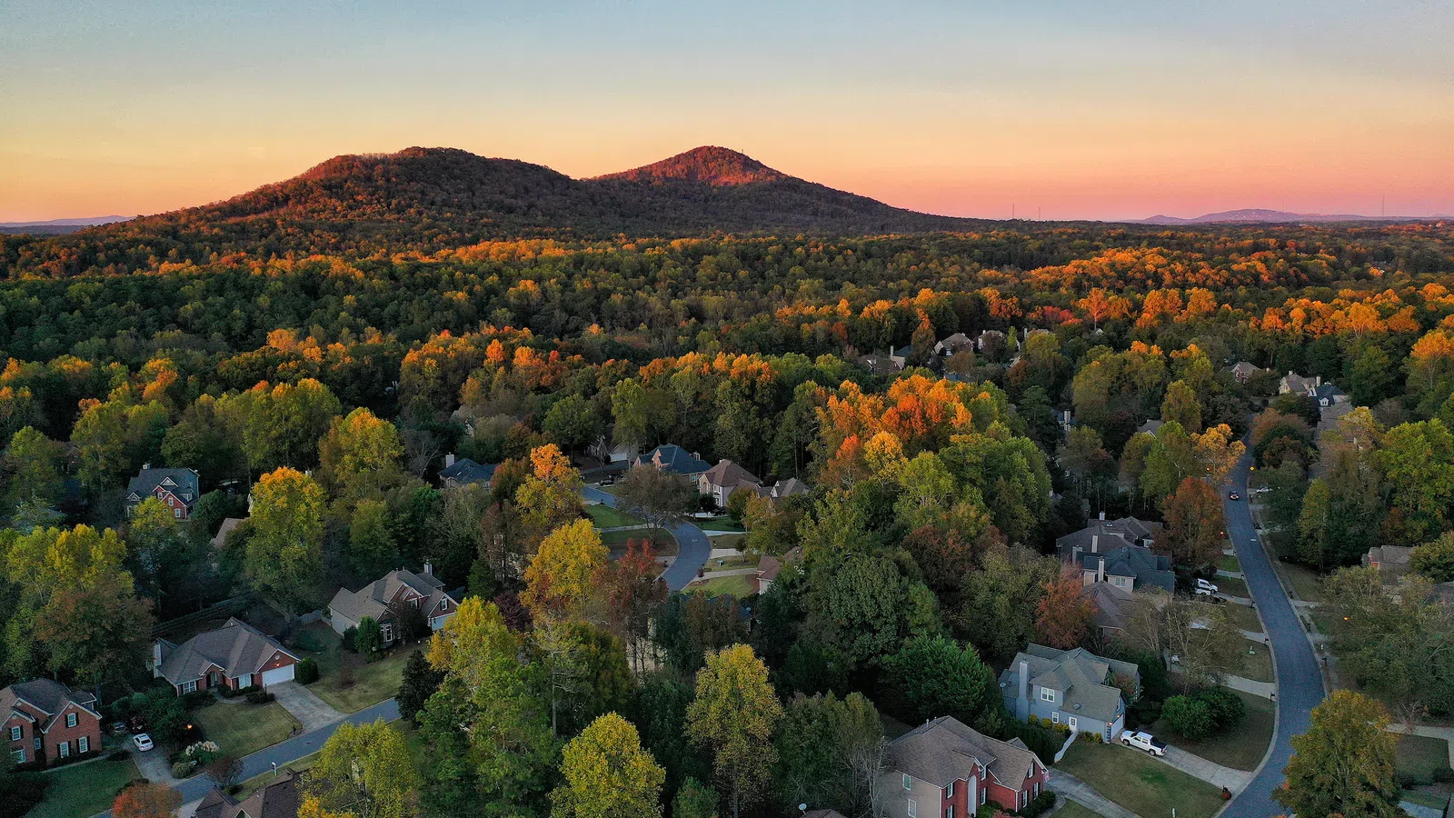 Aerial view of a suburban neighborhood in Kennesaw GA with fall foliage and rolling hills at sunset under a clear sky
