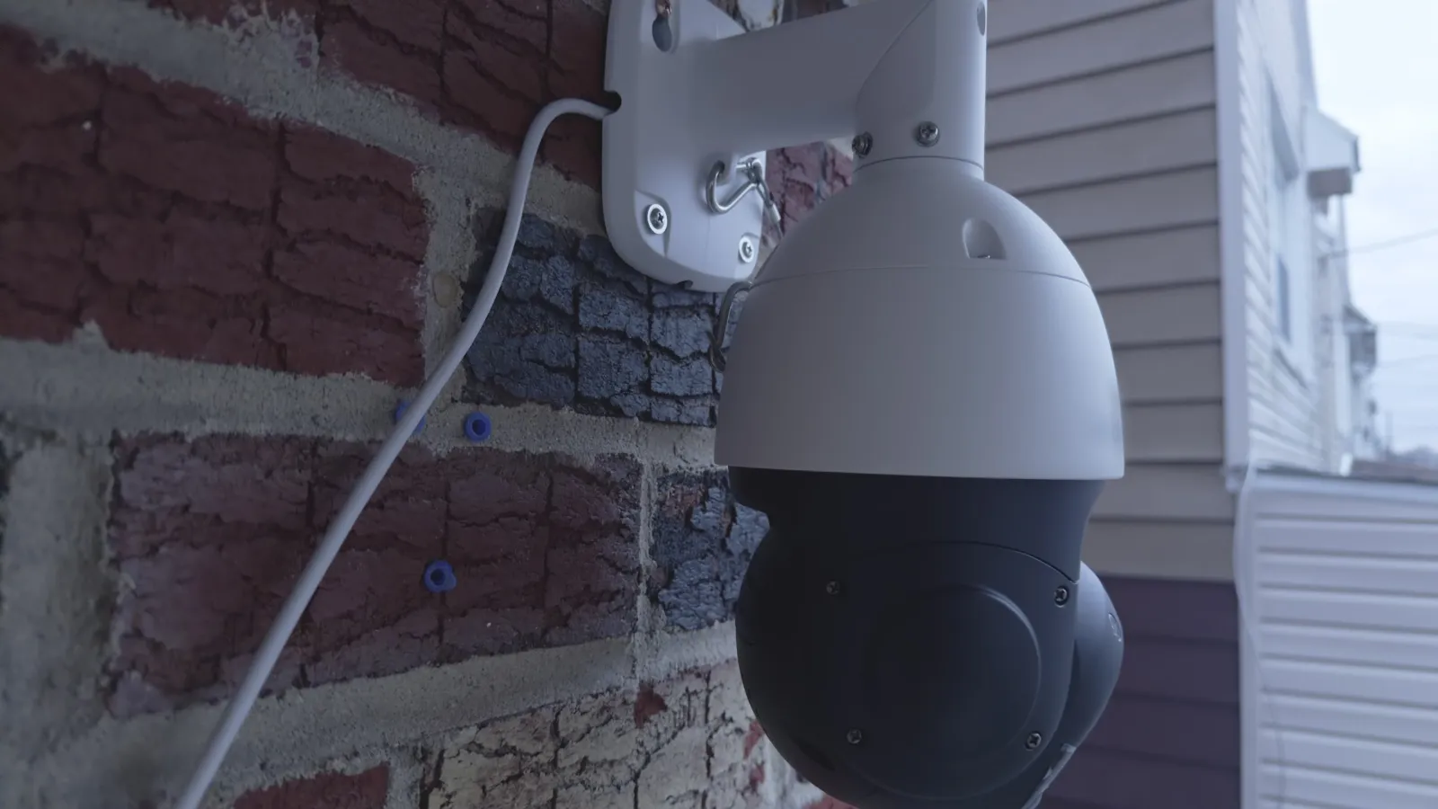 Outdoor dome security camera mounted on brick wall monitoring residential area with connected power cable